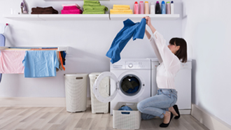 Mulher a tirar uma camisa azul da máquina de secar roupa.